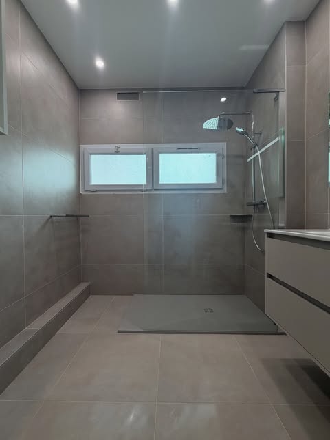 Douche vitrée et grands carreaux gris dans une salle de bain rénovée