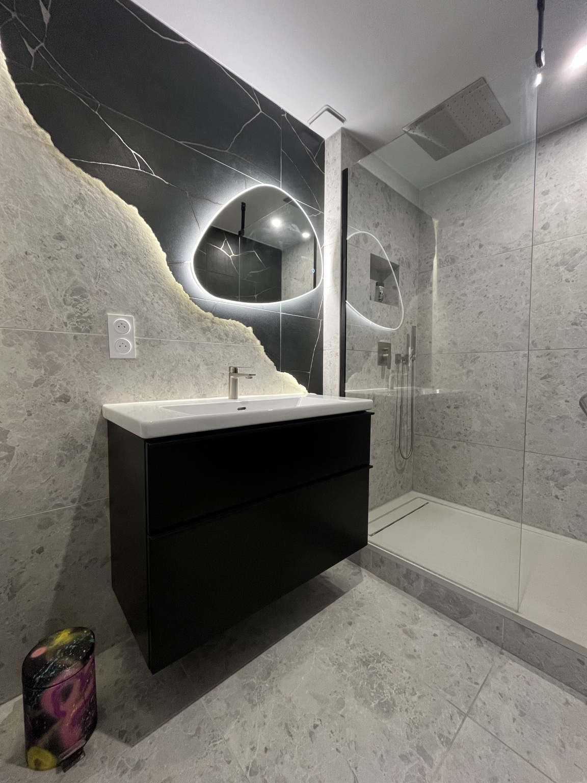 Salle de bain rénovée, vasque blanche, mur sombre et miroir lumineux organique