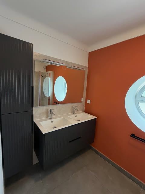 Salle de bain avec mur orange, meuble sombre et miroirs ronds